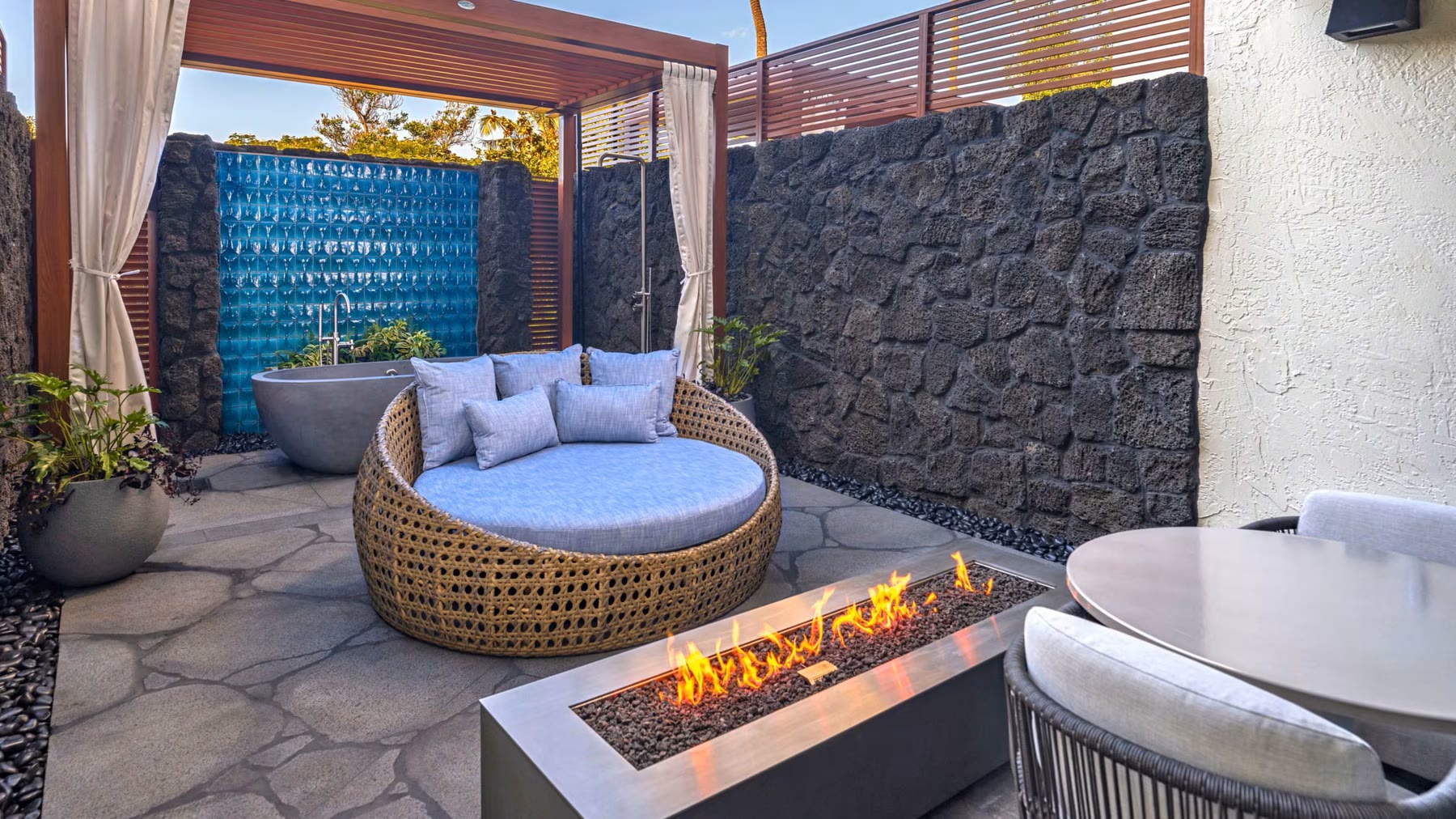 A walled garden courtyard with a fire table, lounge seat and lava-stone wall