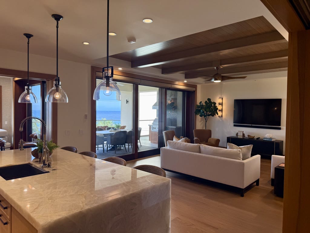 An open great room with a stone-topped island, timber-beamed ceiling and ocean view