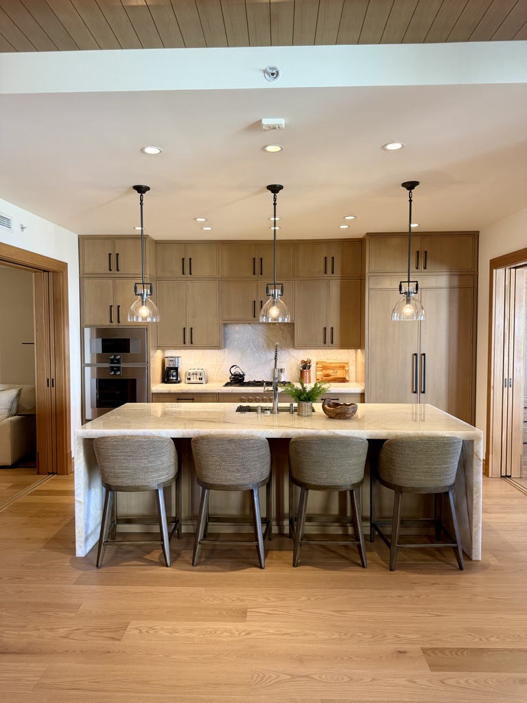 A long kitchen island with four upholstered stools under glass pendants