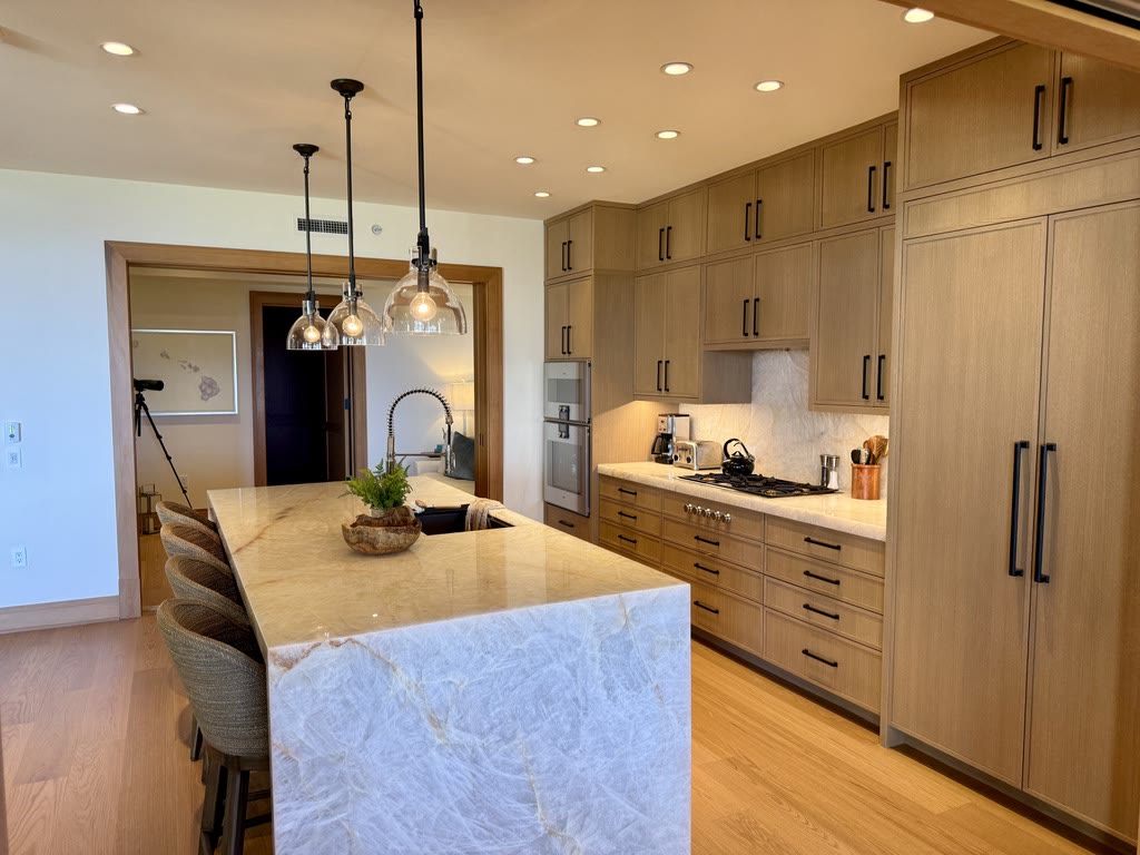 A kitchen in pale oak with a marble waterfall island and glass pendants