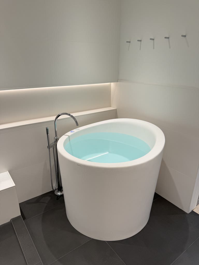 A round white soaking tub on a dark platform in a softly lit bath