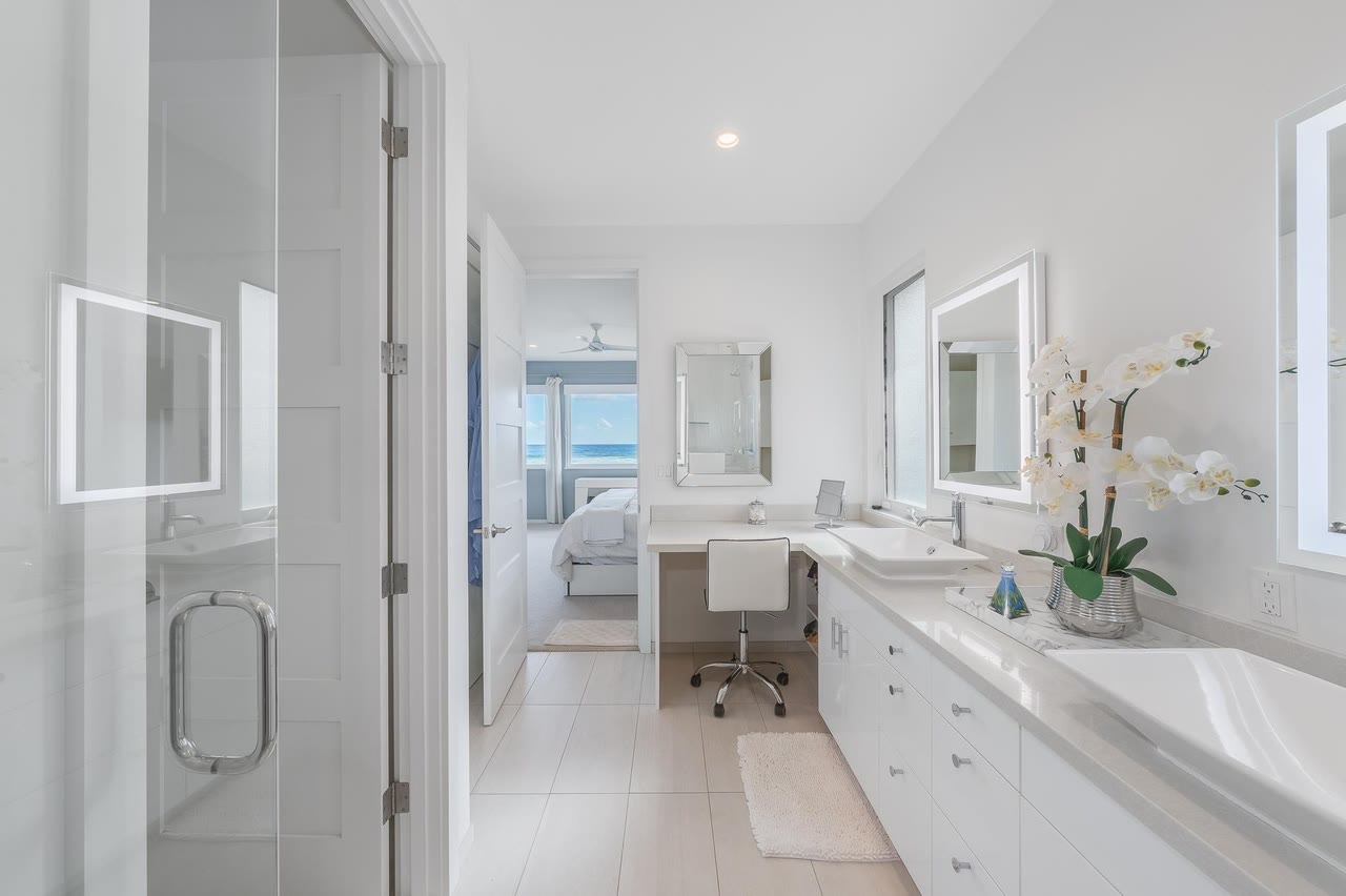 A white primary bath vanity with lit mirrors and orchids