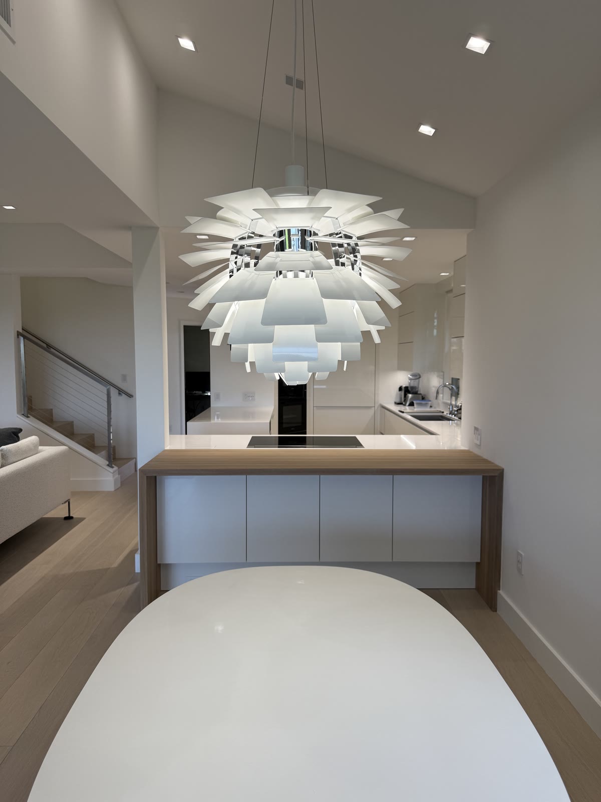 A white dining table under a sculptural artichoke pendant, with the kitchen beyond