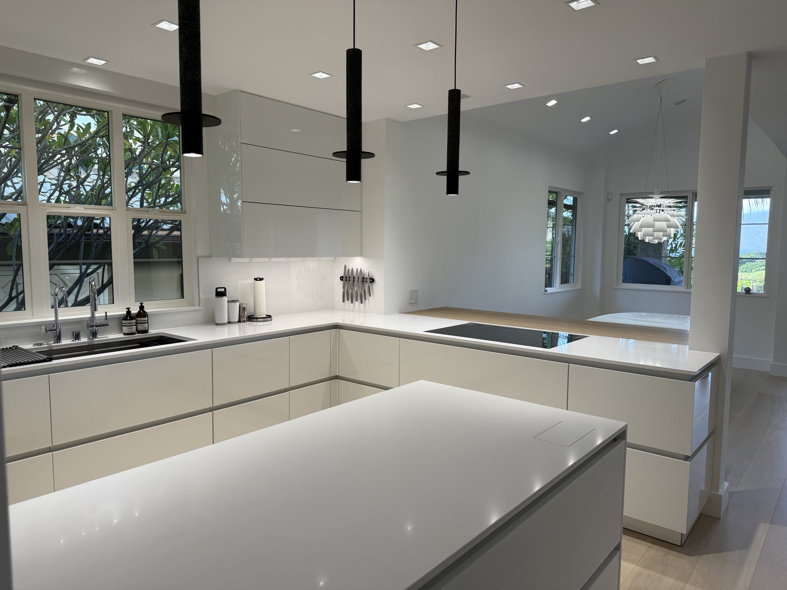 A white kitchen with a quartz island under slim black pendants