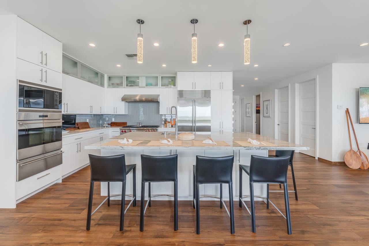 A bright kitchen with a long island and four dark stools