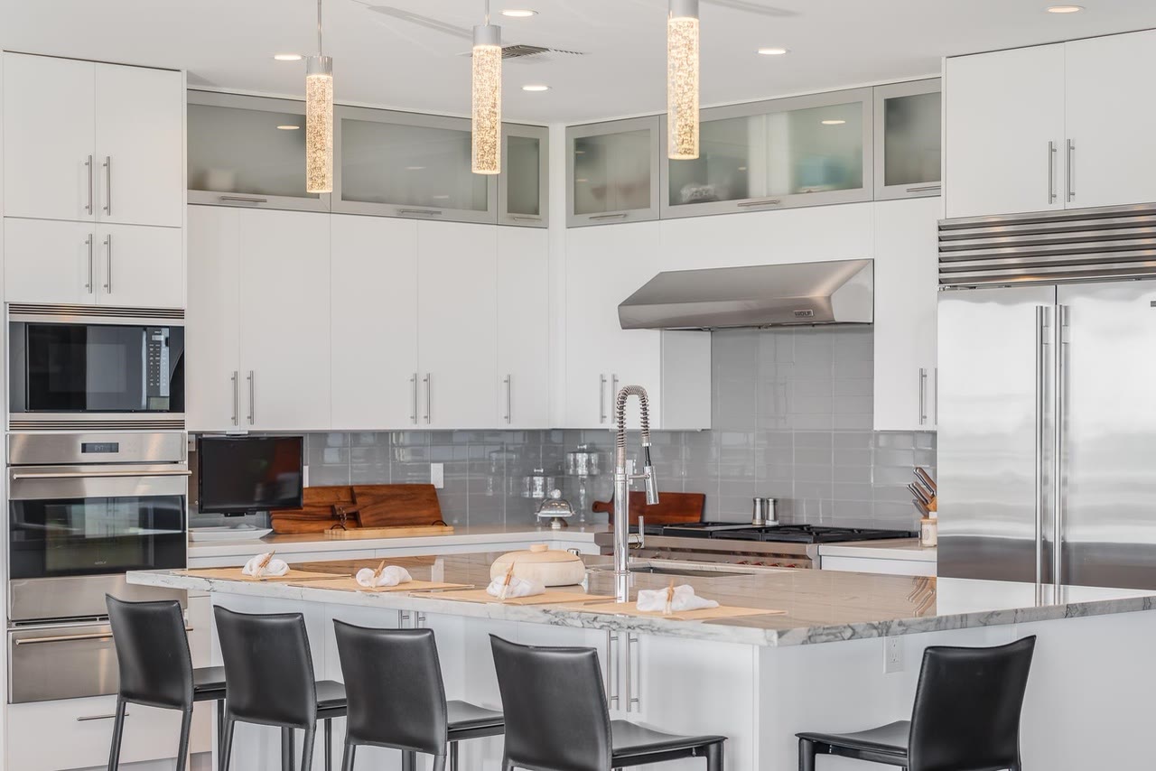 A kitchen island with dark stools in front of stainless wall ovens and a range