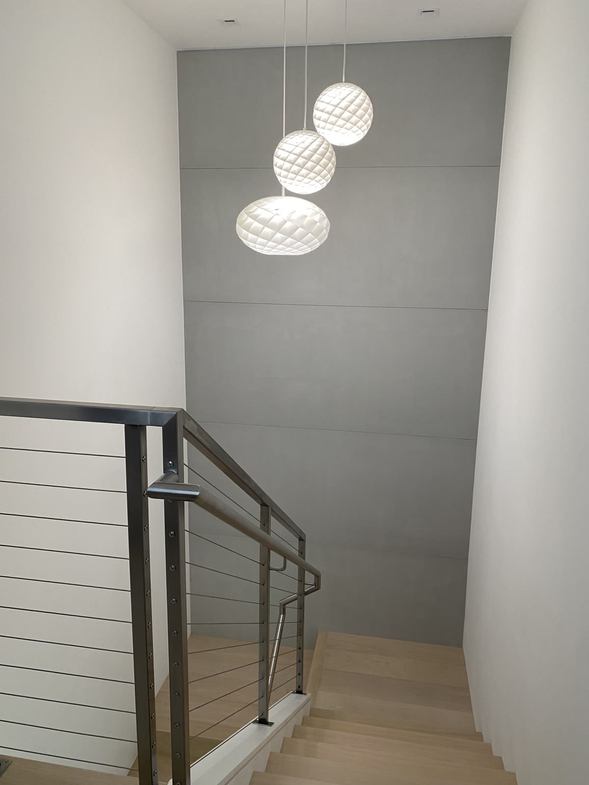 A stairwell with a cable rail and three globe pendants