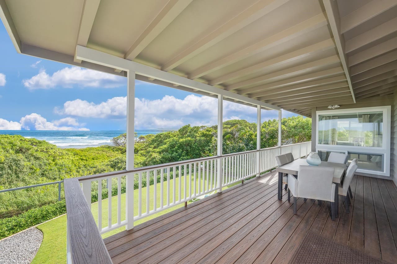 A covered wood-deck lanai looking over green hills to the ocean